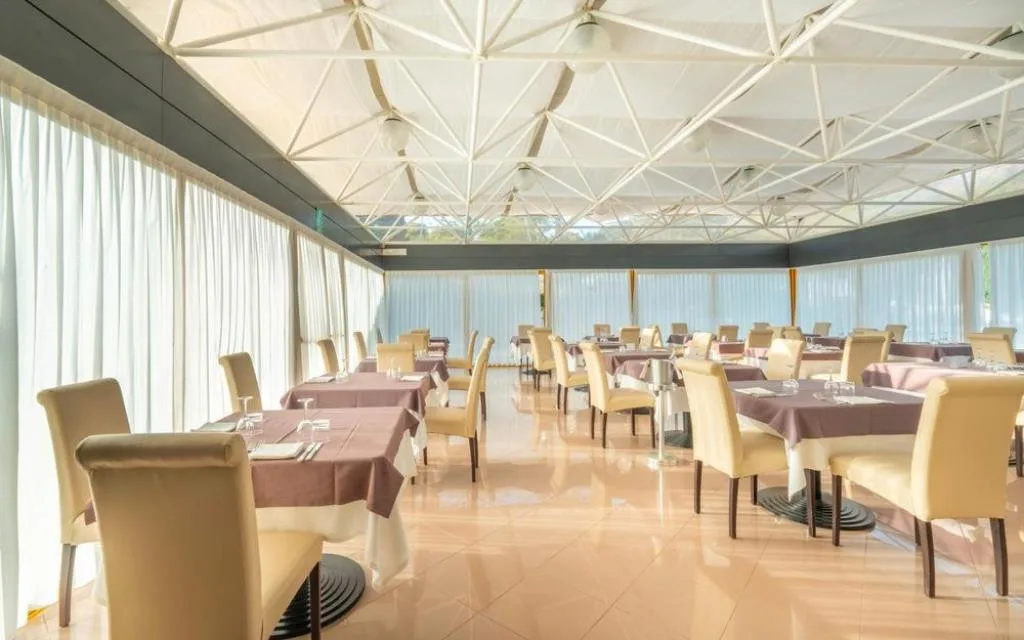 Sala ristorante luminosa con tavoli apparecchiati e ampie vetrate