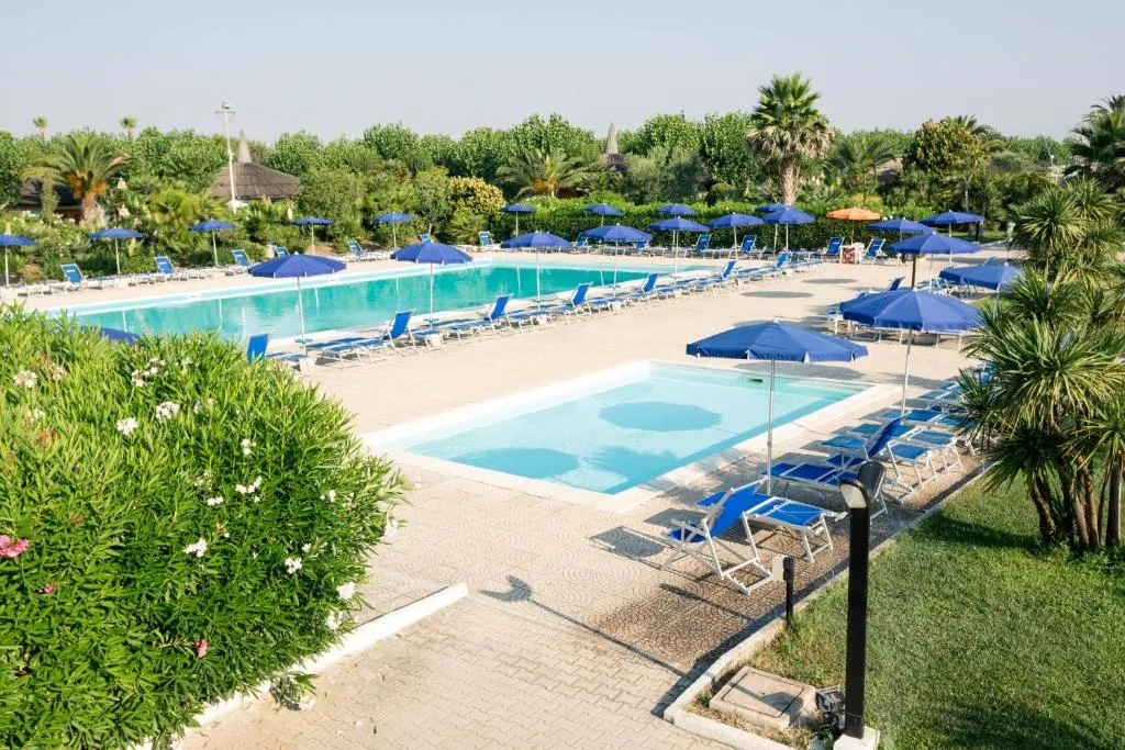 Due piscine con lettini e ombrelloni blu circondate da vegetazione
