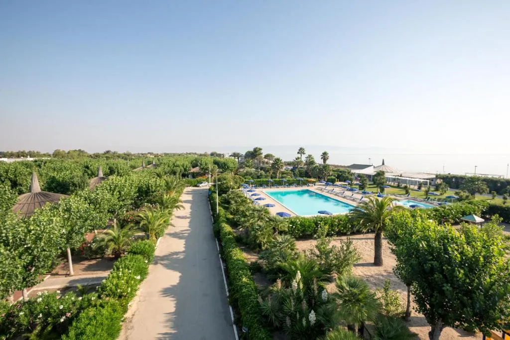 Vista panoramica del resort con viale, piscina e giardino verso il mare
