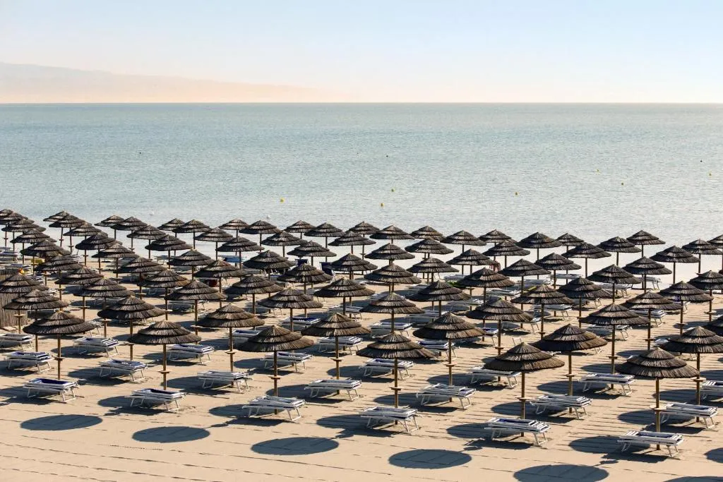 Spiaggia attrezzata con ombrelloni in paglia e lettini affacciata sul mare