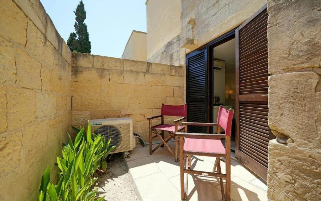 Piccolo patio privato in pietra con sedie regista rosse e ingresso alla camera
