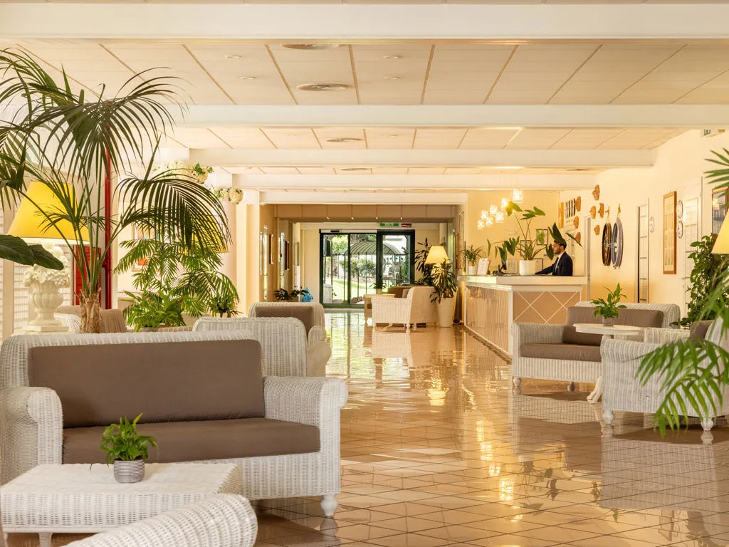Hall luminosa dell'hotel con poltrone in vimini, piante e reception