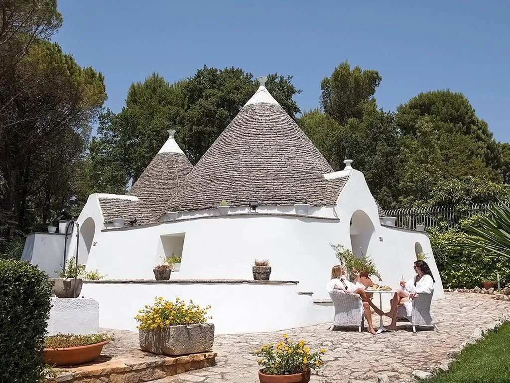Trullo bianco con ospiti sedute al tavolo nel giardino soleggiato