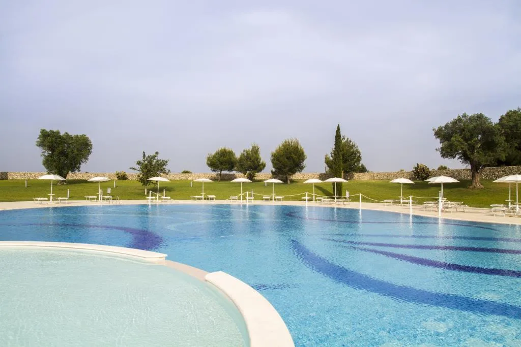 Ampia piscina esterna con lettini, ombrelloni bianchi e prato circostante