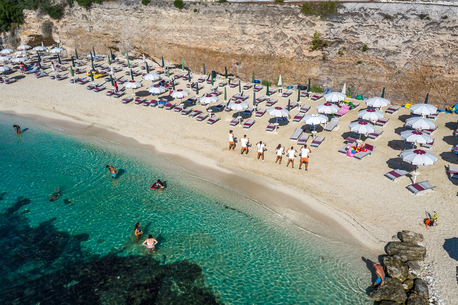 Veduta aerea della spiaggia con ombrelloni, lettini e bagnanti nel mare cristallino