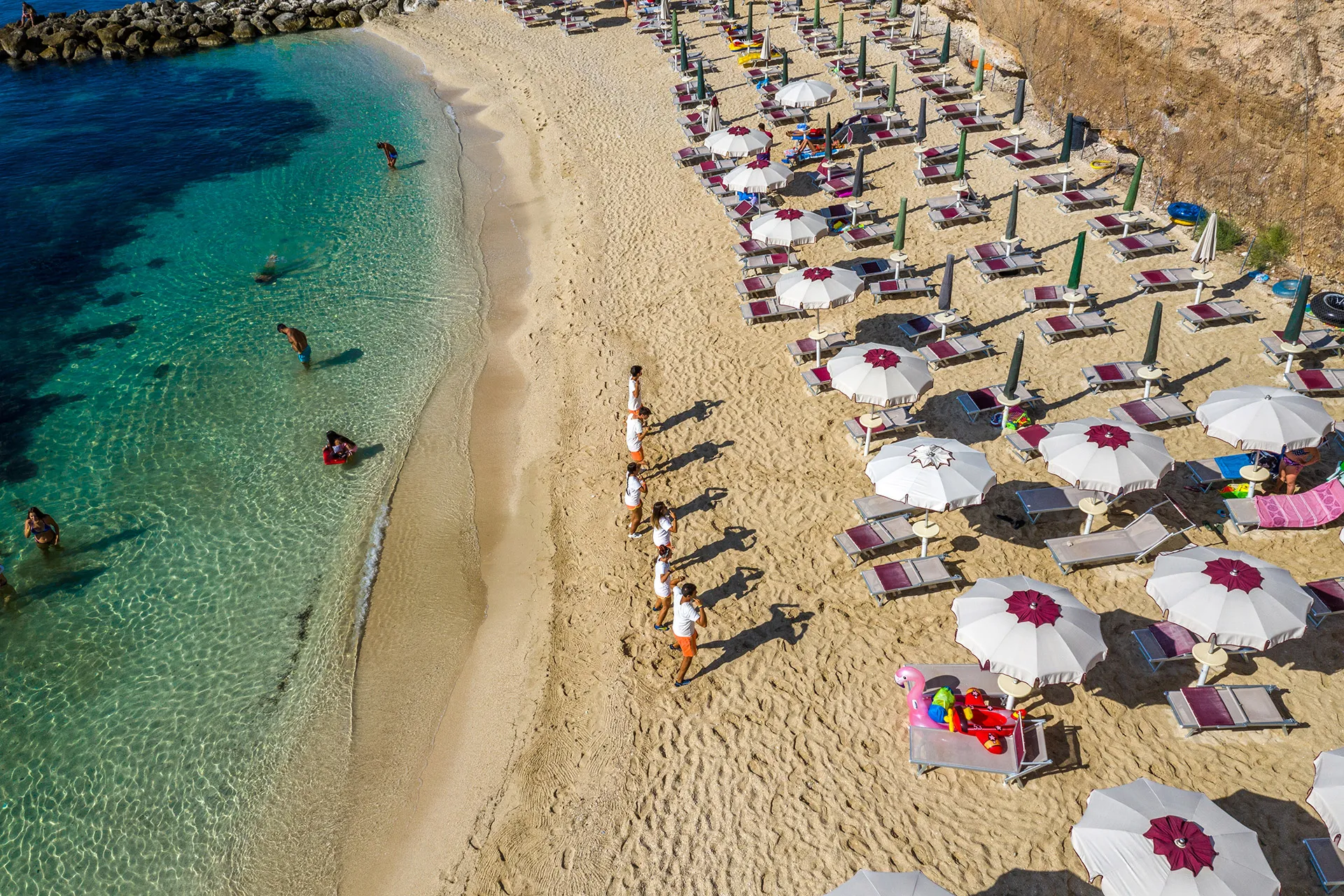 Spiaggia con ombrelloni e lettini lungo il mare azzurro con bagnanti e animatori