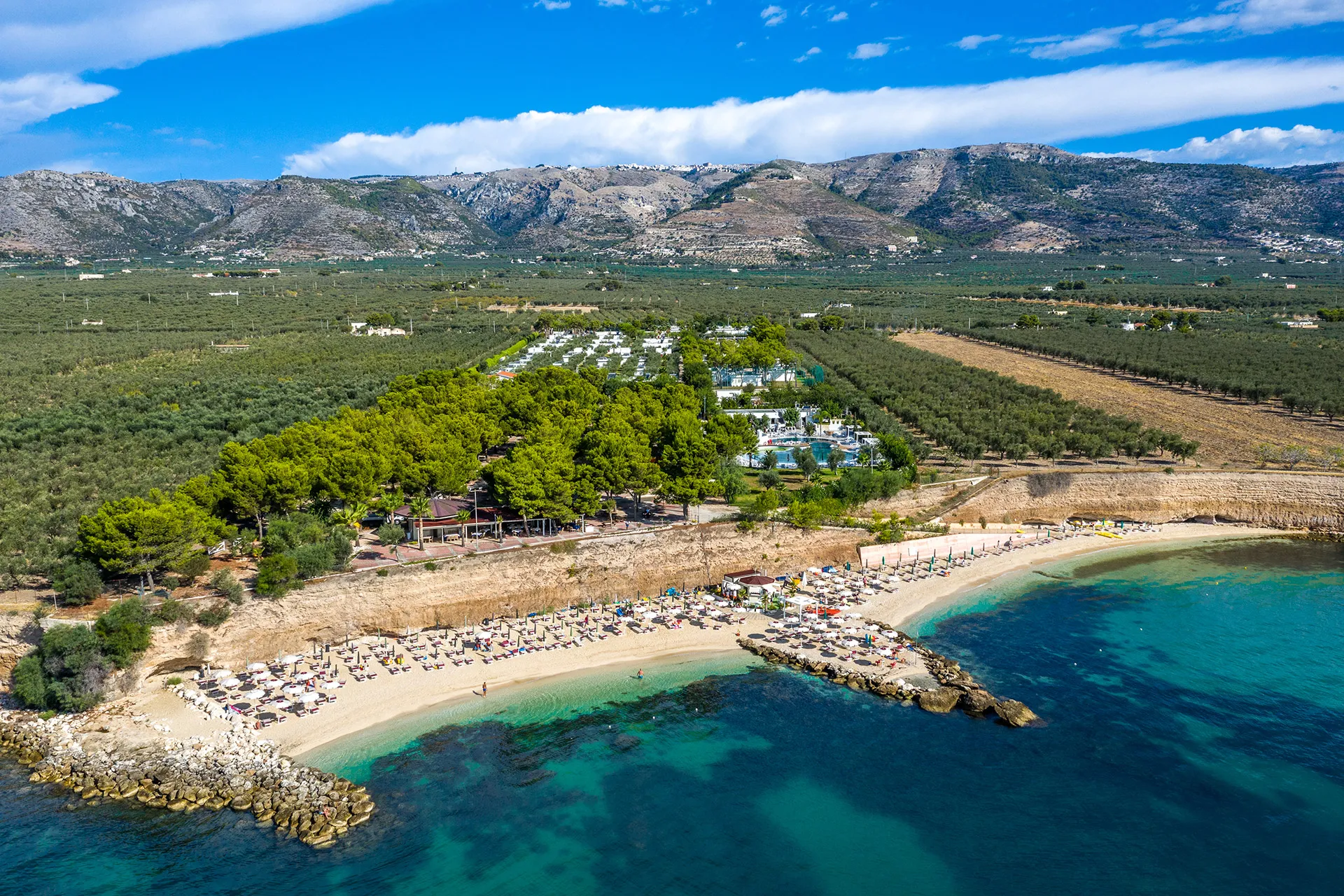 Vista aerea della spiaggia e del villaggio immerso nel verde con montagne sullo sfondo