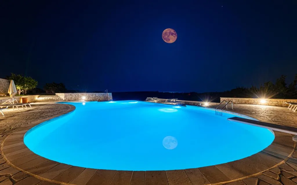 Piscina illuminata di notte con luna piena e cielo stellato