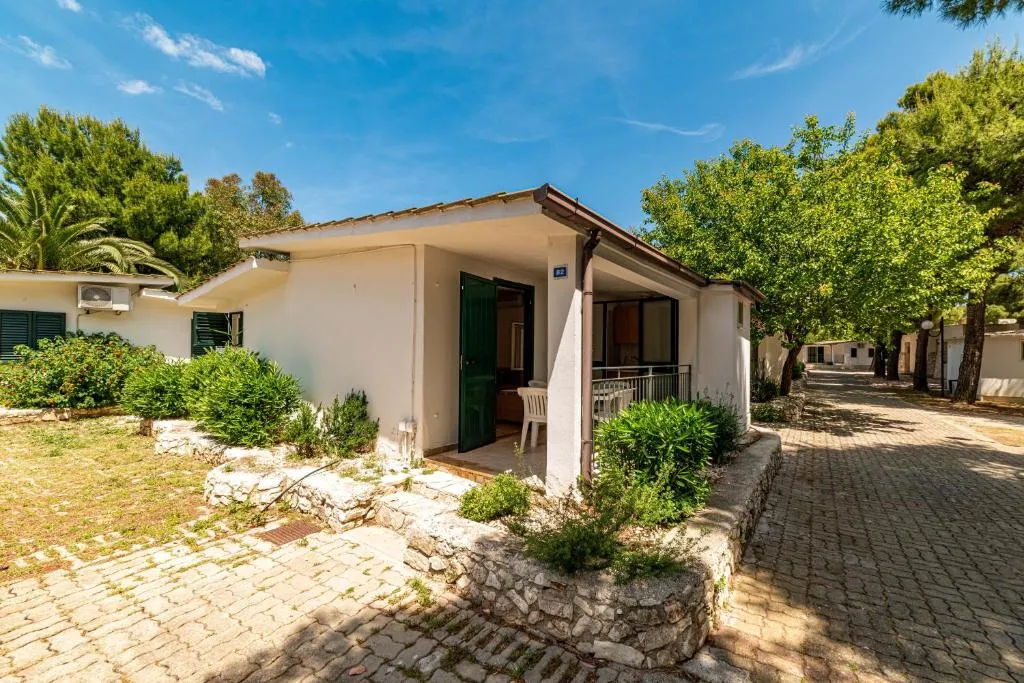 Bungalow bianco con portico e piccolo giardino lungo il vialetto