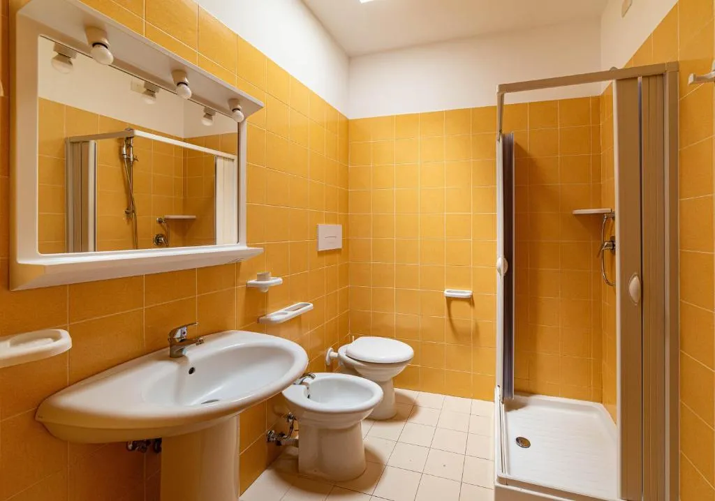 Bagno con piastrelle arancioni, doccia, lavabo e sanitari