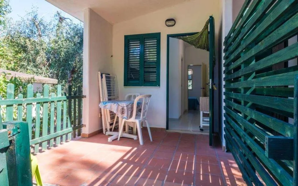 Veranda esterna con tavolino, sedie e ingresso al bungalow immerso nel verde