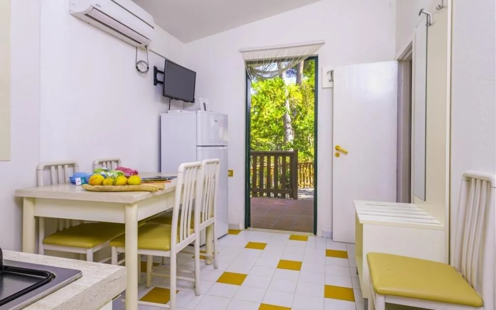 Cucina e zona pranzo con tavolo, frigorifero e uscita sul verde
