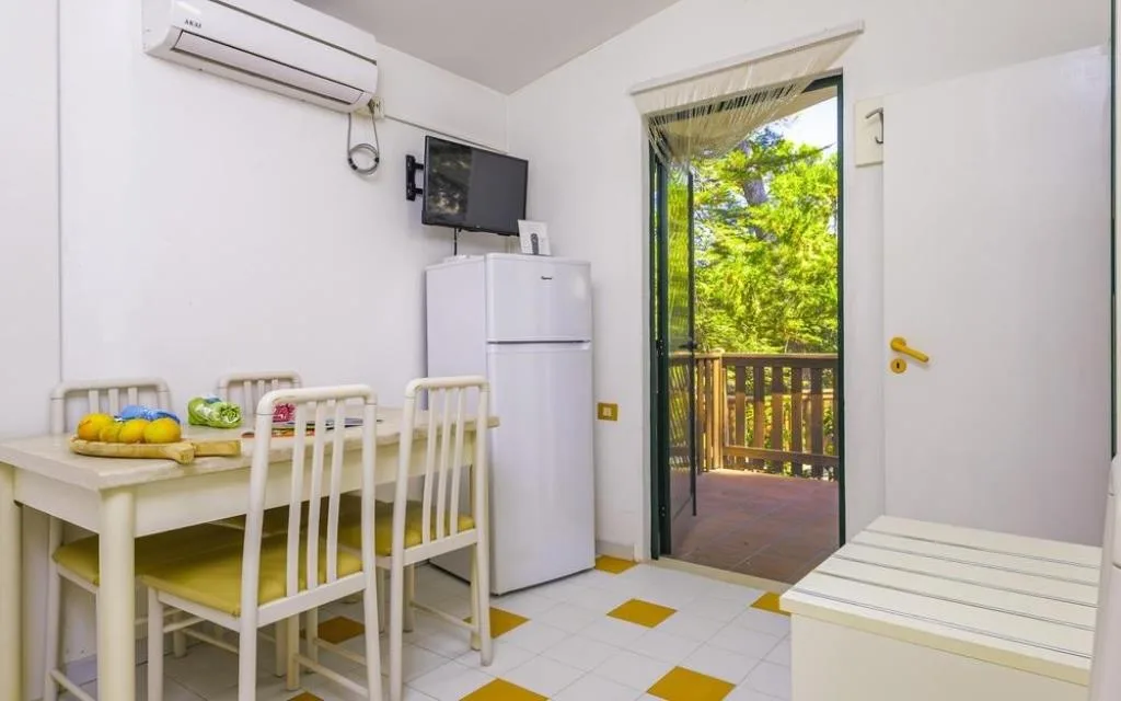 Zona pranzo con tavolo, sedie, frigorifero e uscita sulla veranda