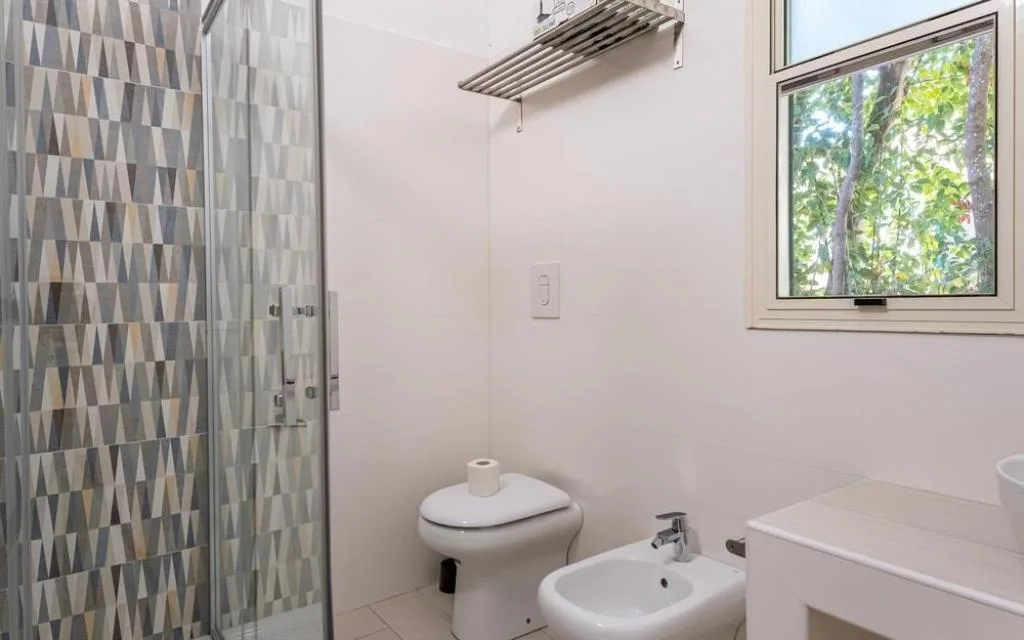 Bagno bianco con doccia, WC, bidet e finestra sul verde