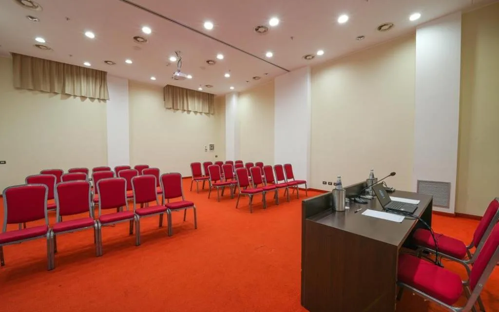 Sala riunioni con sedie rosse disposte a platea e postazione relatore