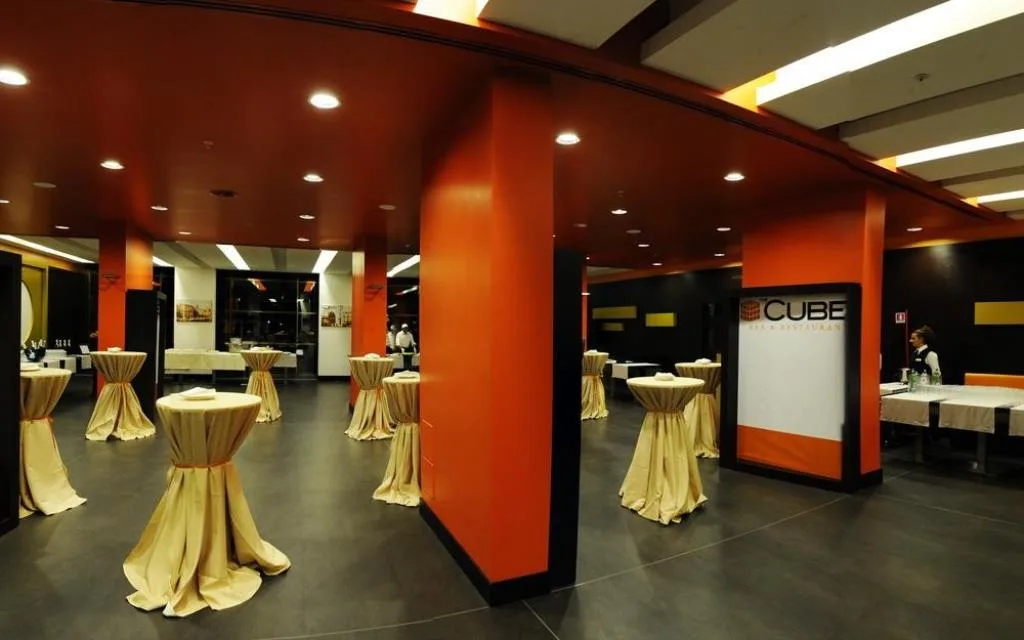 Area bar e ristorante Cube con tavoli alti drappeggiati e pareti arancioni