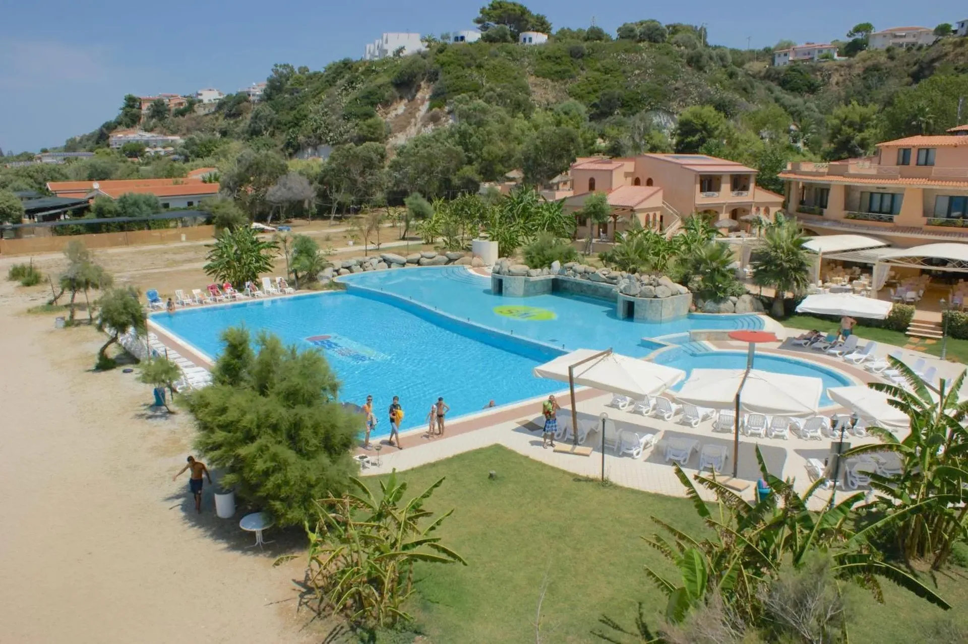 Ampia piscina del resort con vasca per bambini, lettini e ospiti, circondata da palme e vegetazione