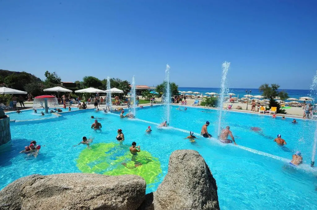 Piscina con giochi d'acqua e fontane, bagnanti in acqua e vista sul mare sullo sfondo
