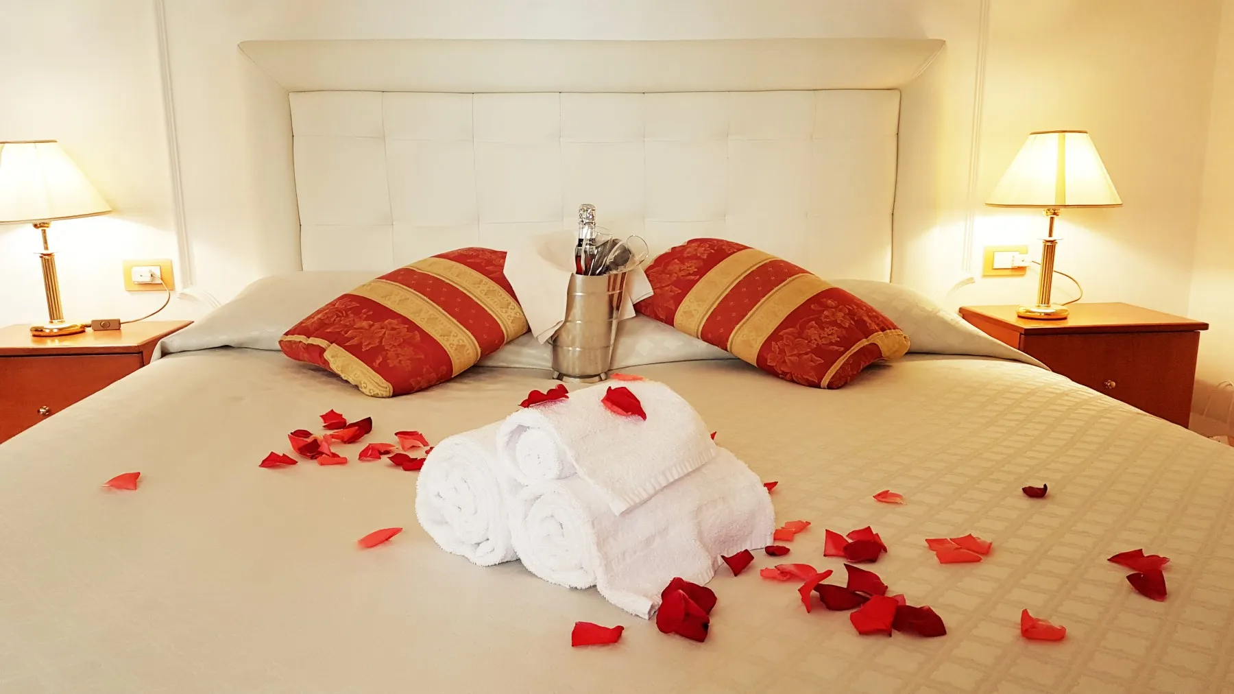 Letto matrimoniale con allestimento romantico, petali di rosa, asciugamani e spumante