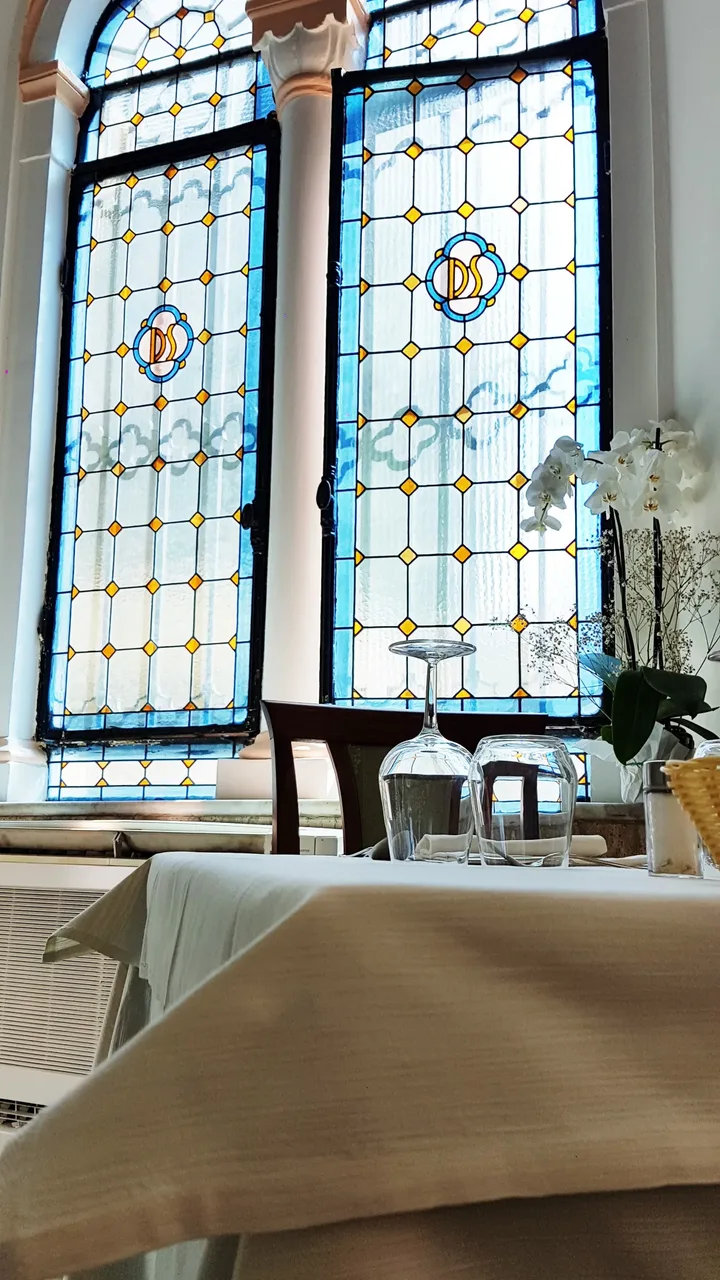 Sala ristorante con grandi vetrate decorate in stile liberty e tavoli apparecchiati