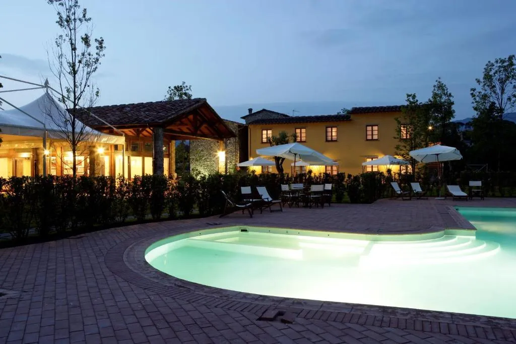 Piscina illuminata al crepuscolo con vista sul casale e ombrelloni