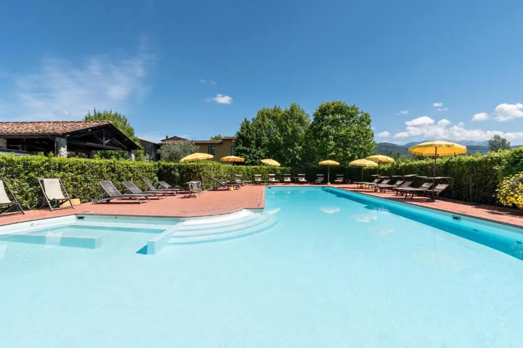 Grande piscina azzurra con ombrelloni gialli e vista sulle montagne