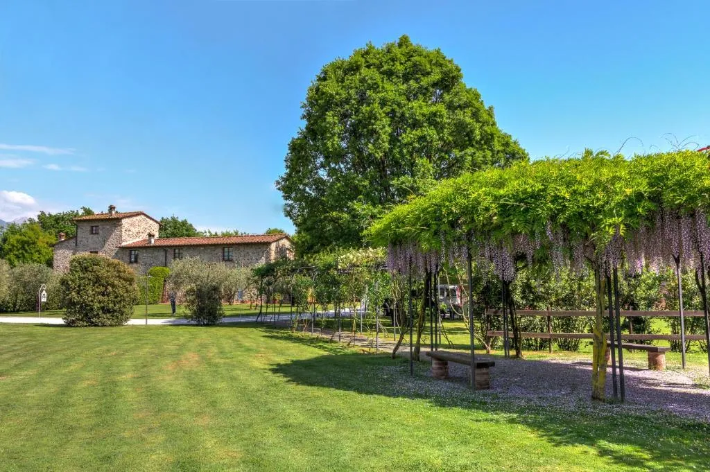 Giardino con casale in pietra e pergolato di glicine in fiore