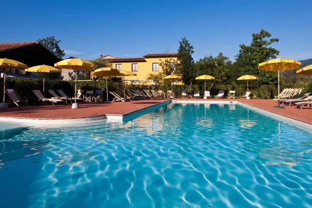 Piscina azzurra con lettini e ombrelloni gialli davanti al casale