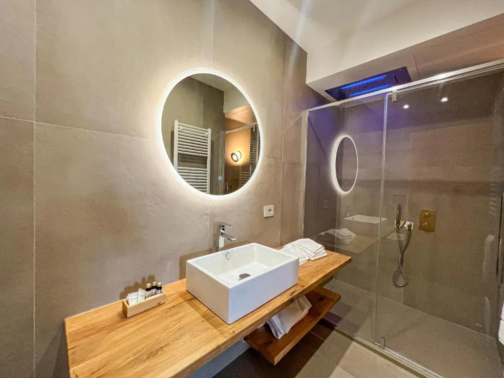 Bagno moderno con lavabo in legno, specchio rotondo e doccia in vetro