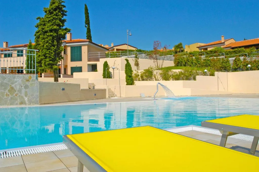 Piscina con lettini gialli e residence con cielo azzurro sullo sfondo