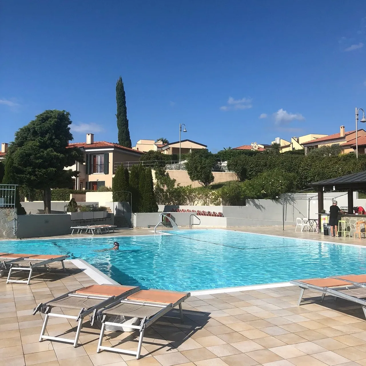 Piscina con lettini, ombrelloni e bar sullo sfondo del residence