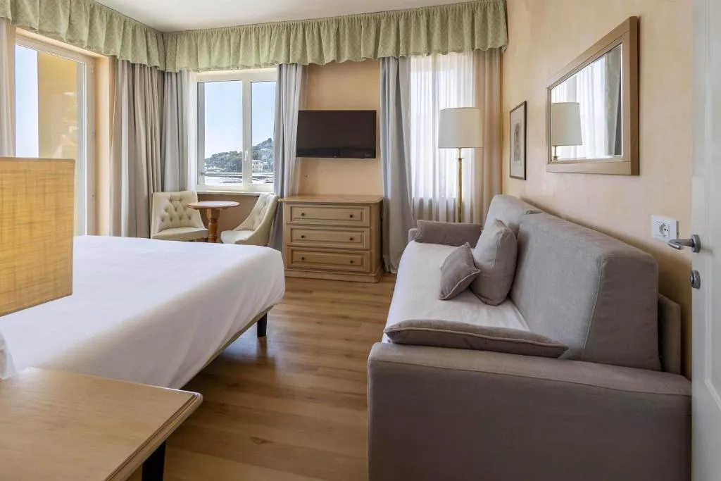 Camera con letto, divano grigio, TV e finestre con vista sulla costa