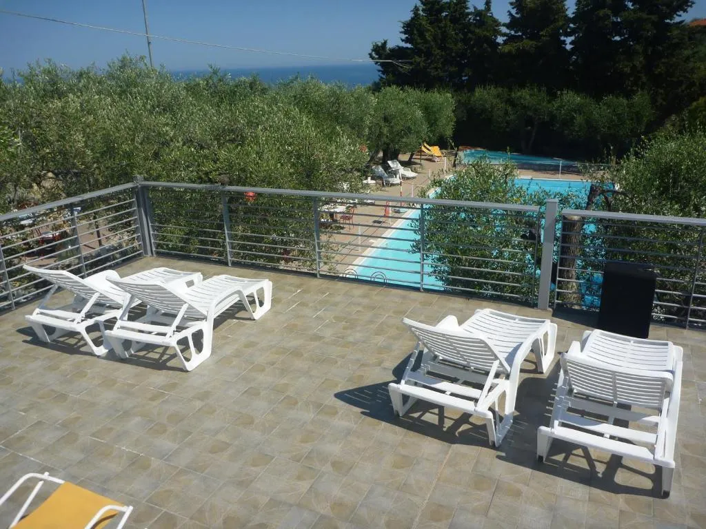 Terrazza con lettini bianchi e vista sulla piscina e sul mare tra gli ulivi
