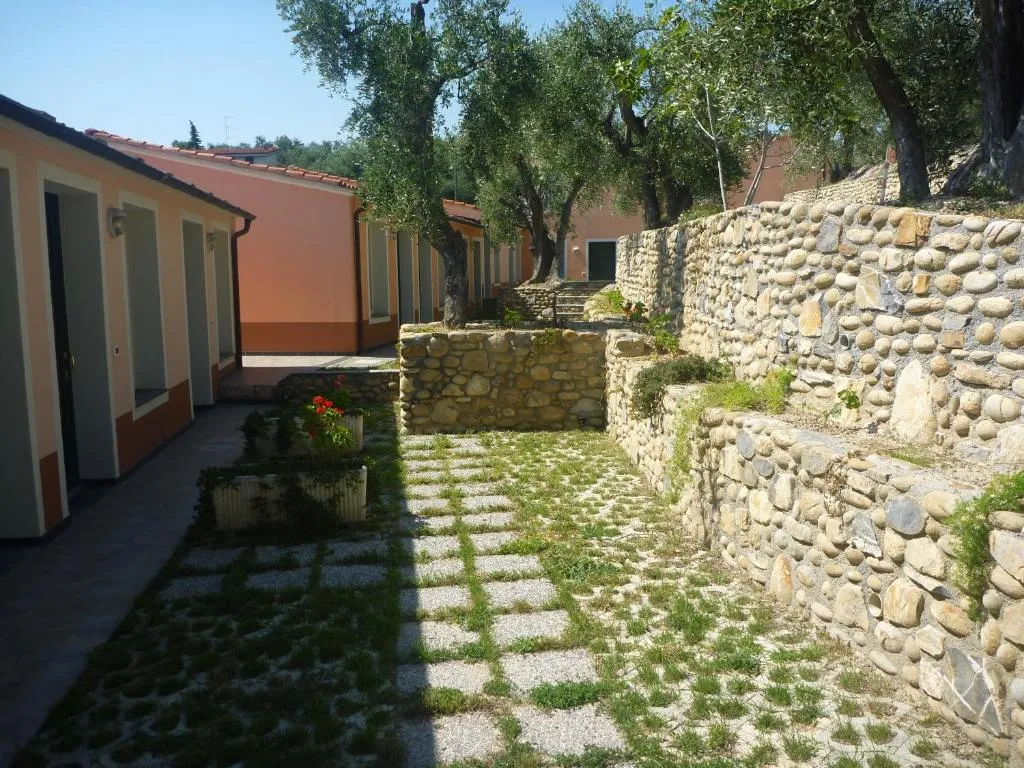 Vialetto esterno con edifici rosa, muri in pietra e giardino con ulivi