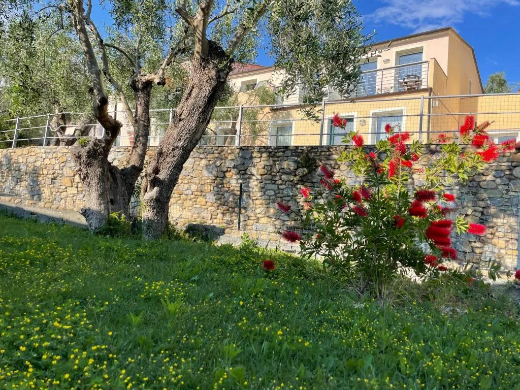 Muro in pietra con ulivi e fiori rossi e edificio giallo sullo sfondo