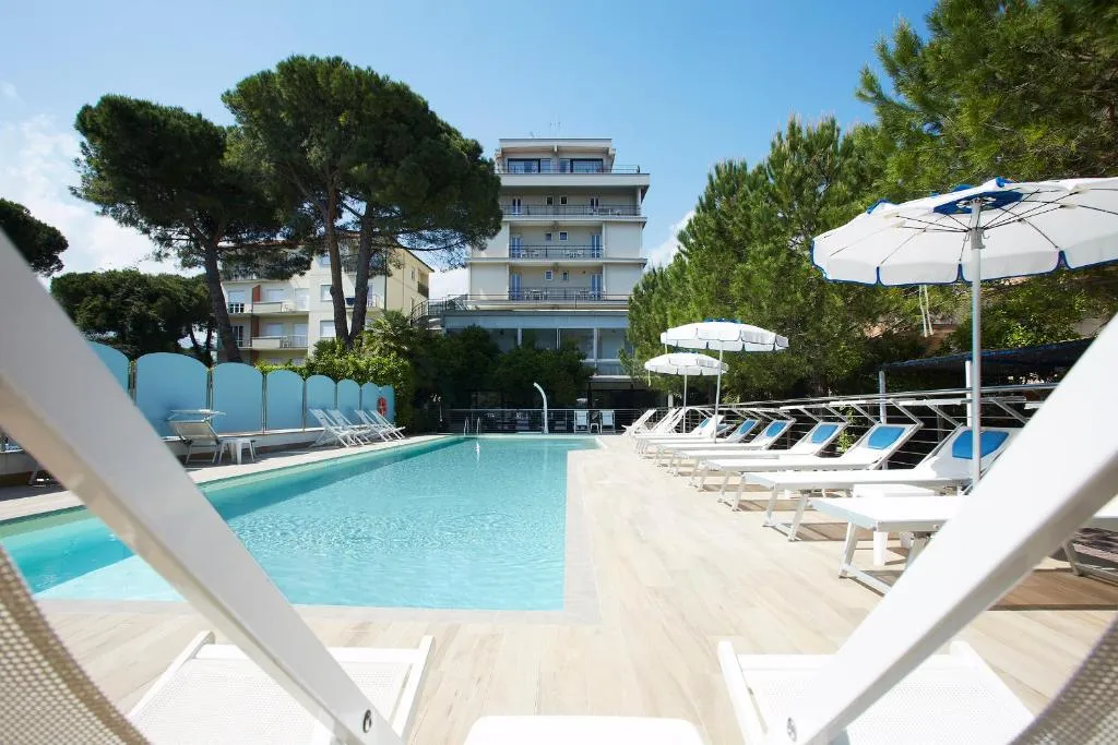 Piscina con lettini bianchi e ombrelloni e hotel sullo sfondo