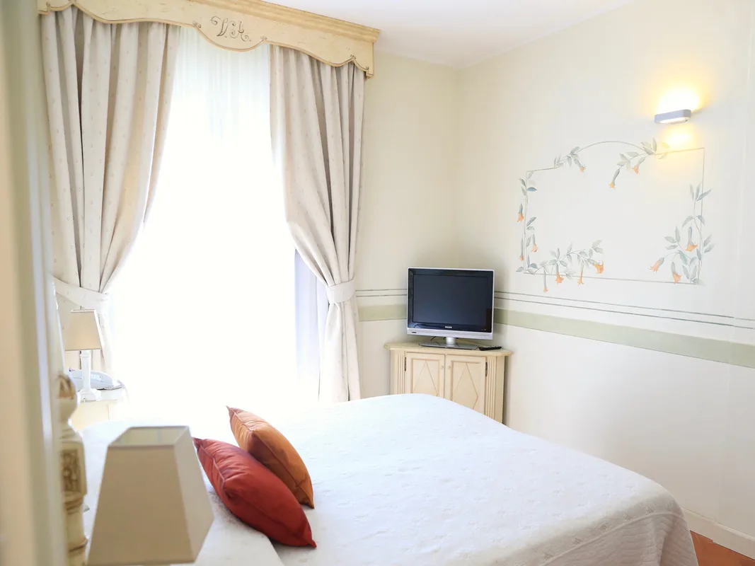 Camera matrimoniale con TV, decorazioni floreali a parete e cuscini colorati sul letto