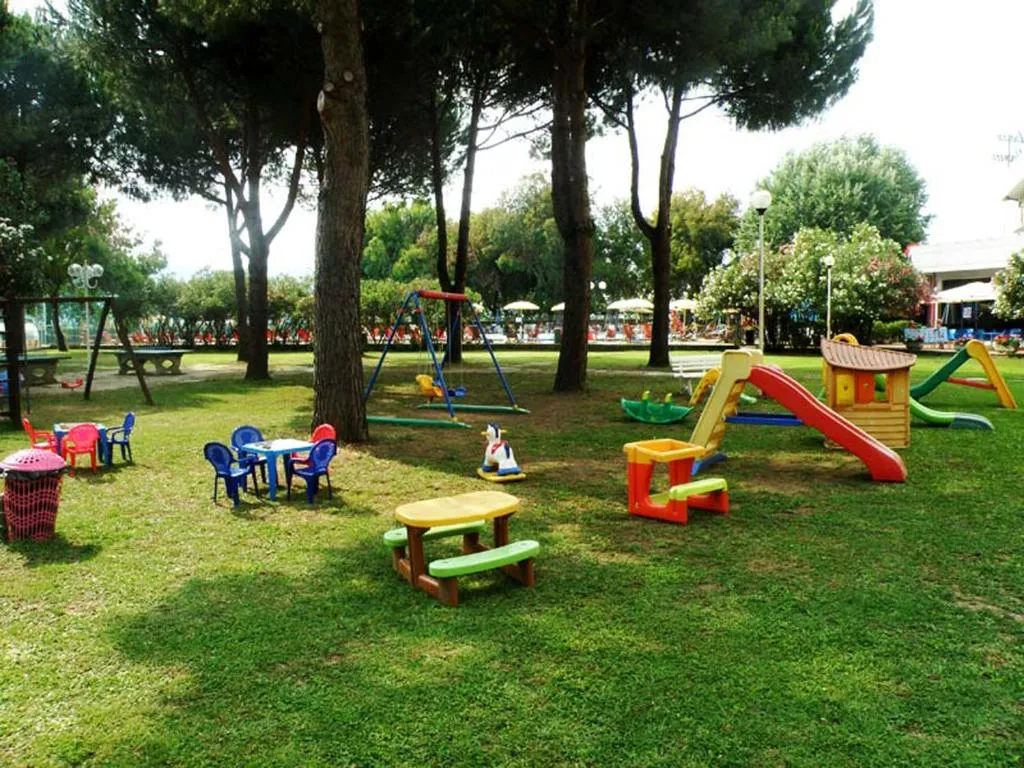 Area giochi per bambini nel giardino con scivoli colorati, altalene e tavolini sotto i pini