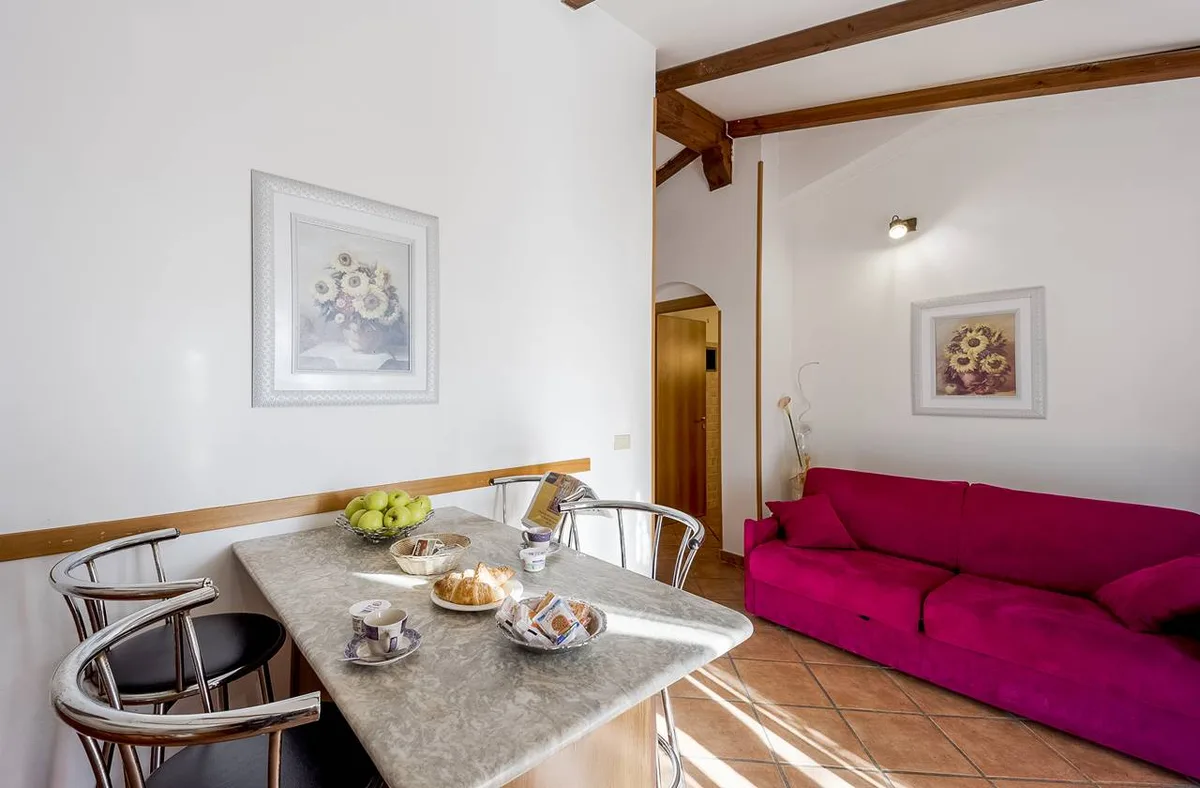 Soggiorno luminoso con tavolo, divano fucsia e quadri con fiori alle pareti