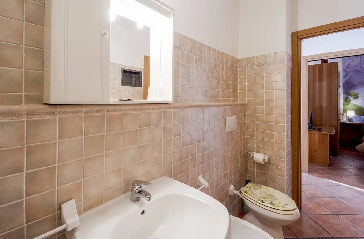 Bagno con piastrelle beige, lavabo, specchio e WC