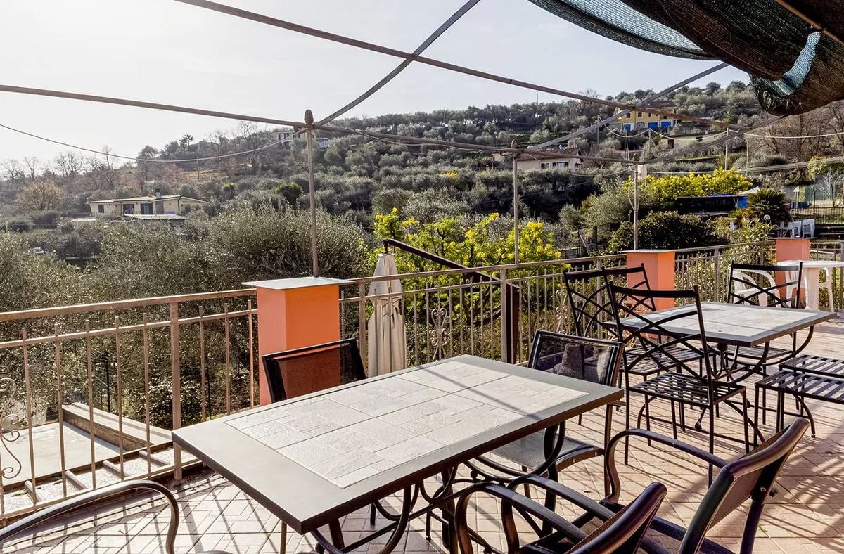 Terrazza con tavoli e sedie in ferro affacciata sulle colline con uliveti