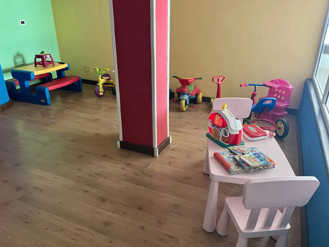 Sala giochi per bambini con tricicli, tavolini e pavimento in legno