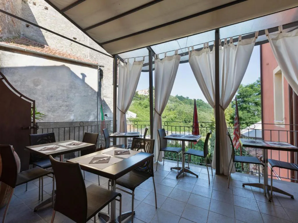 Sala ristorante coperta con tavoli, tende bianche e vista sulle colline