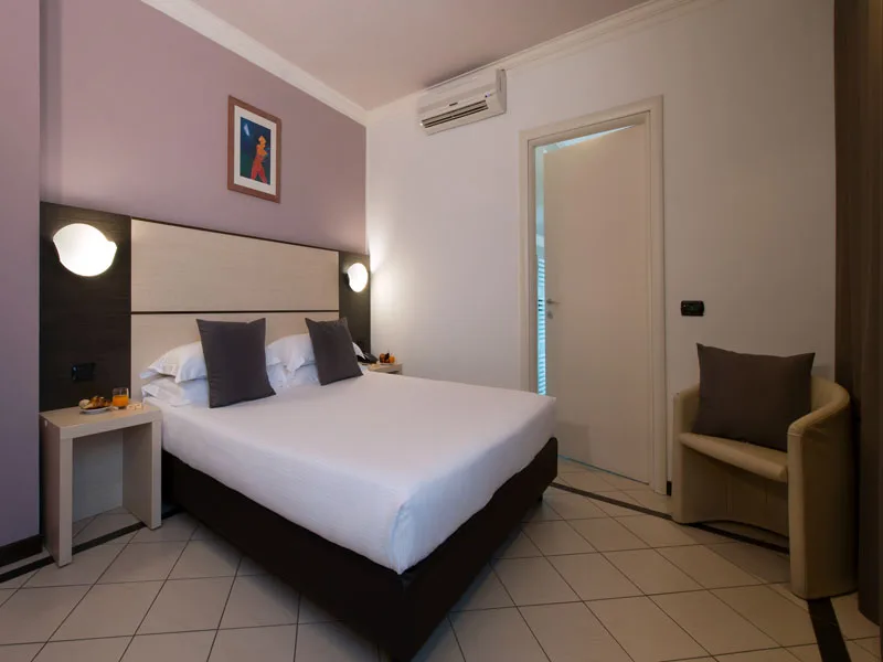 Camera matrimoniale con cuscini grigi, poltrona e accesso al bagno