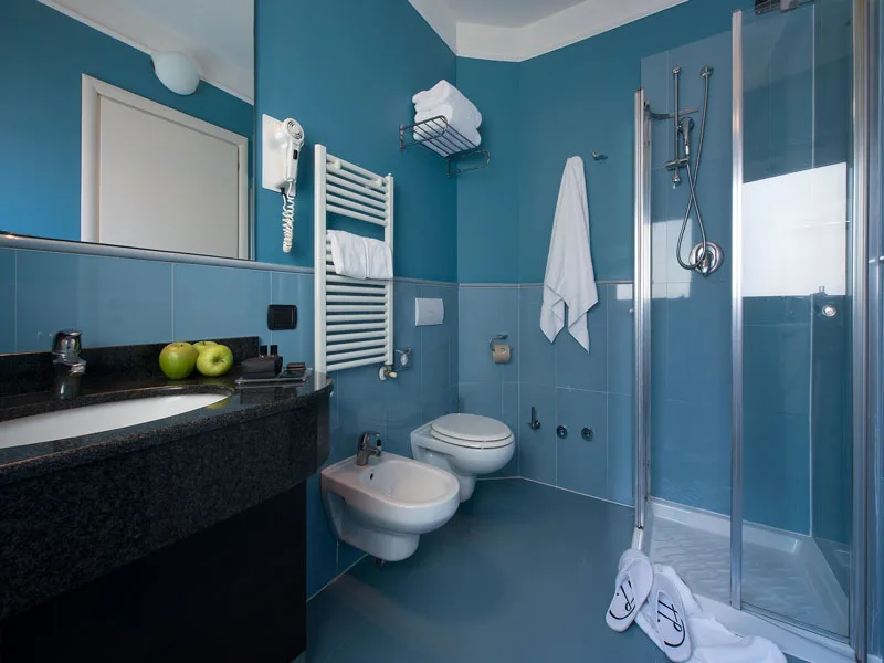 Bagno azzurro con doccia, lavabo in pietra scura, bidet e scaldasalviette