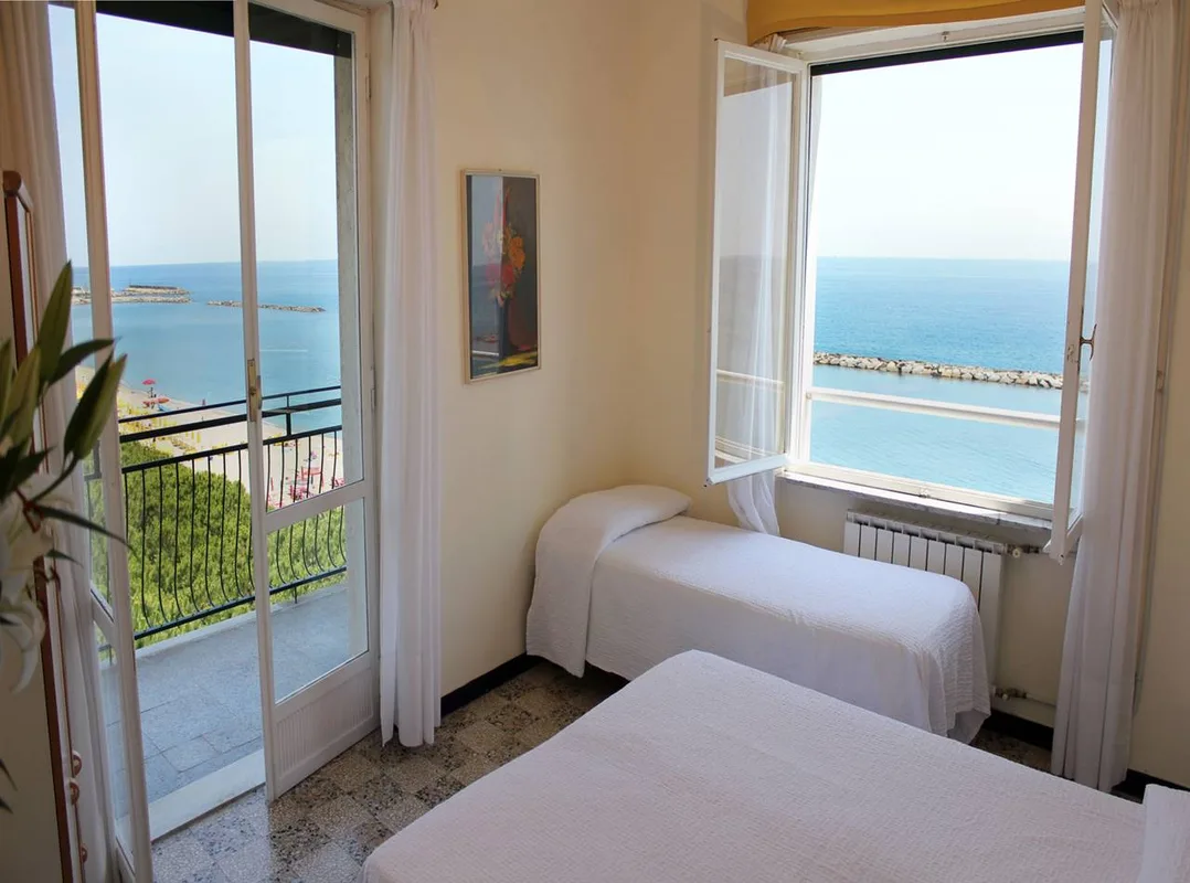 Camera con due letti singoli, balcone e ampie finestre con vista sul mare