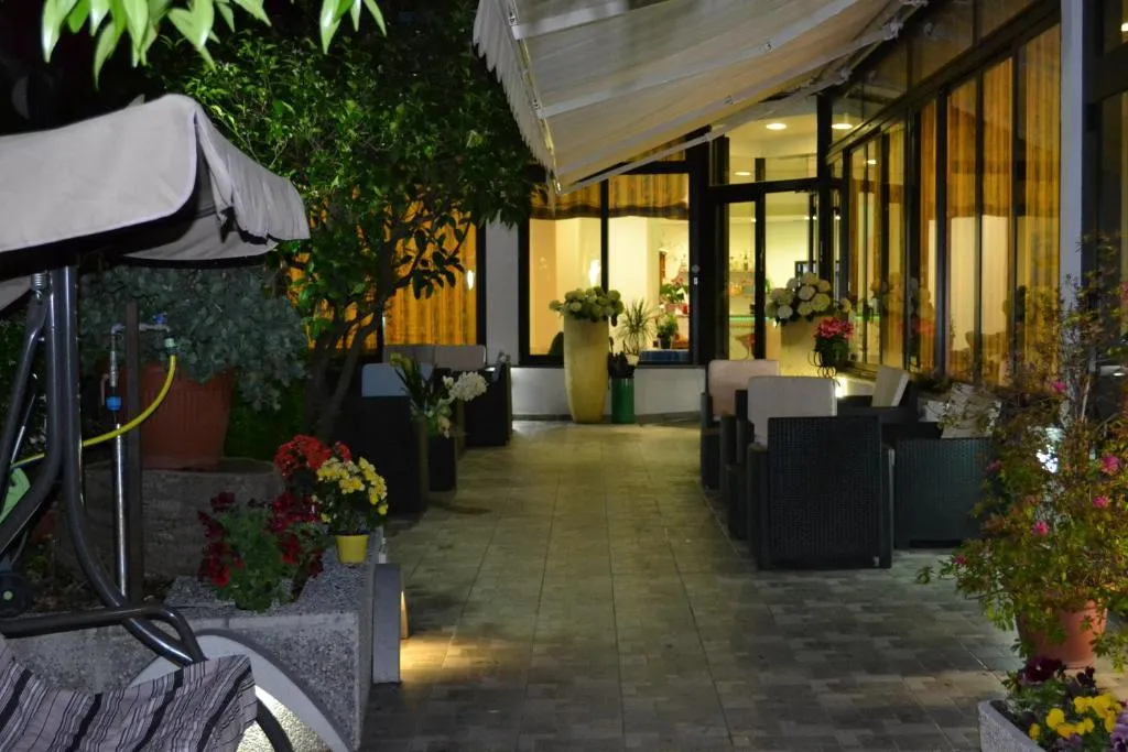 Terrazza esterna illuminata di sera con poltrone, fiori e vista sulla hall