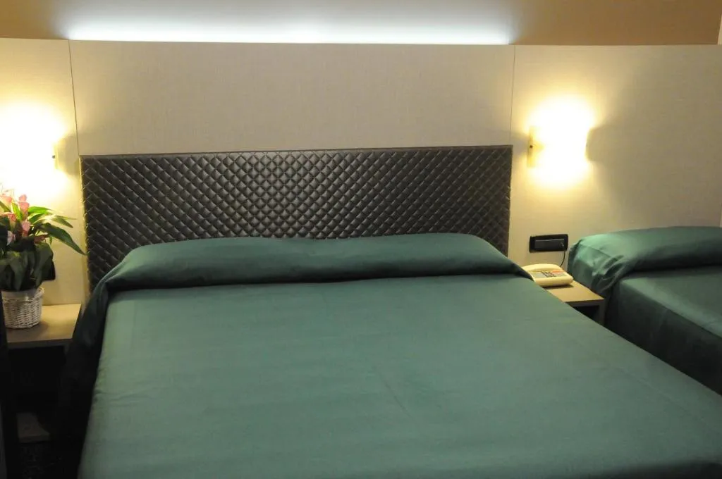 Camera con letti accostati dalla coperta verde, testiera trapuntata e applique alle pareti