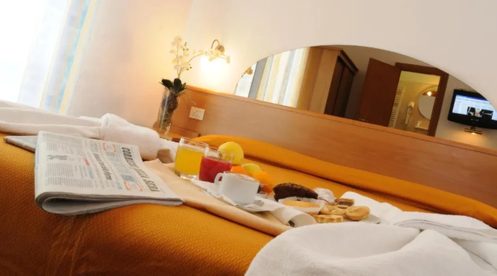 Colazione servita a letto su vassoio con succhi, cornetti e biscotti, in camera dai toni arancioni
