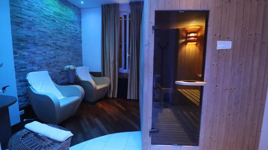 Zona relax della spa con poltrone, parete in pietra e accesso alla sauna in vetro
